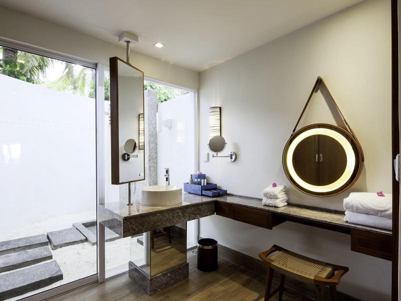 Helles Badezimmer mit großer Glasdusche, hölzernem Waschbecken, rundem Spiegel und Handtüchern.