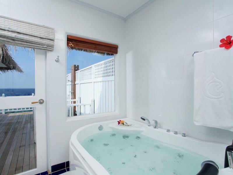 Helles Badezimmer mit weißer Badewanne, Fenster, Tür zum Meer und Handtuch mit roter Blume.