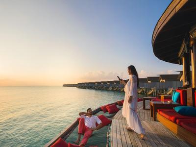 Zwei Personen entspannen auf einer Terrasse mit Blick auf das Meer bei Sonnenuntergang.