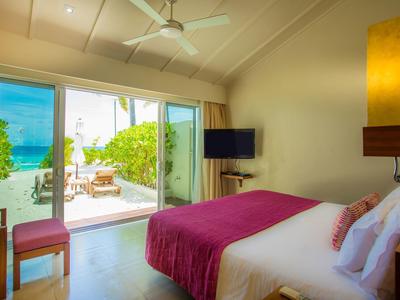 Helles Hotelzimmer mit Doppelbett, pinker Decke und Blick auf Terrasse mit Meer.