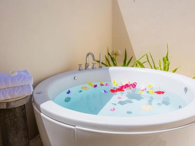 Runde Badewanne mit Wasser und Blüten, daneben Handtücher auf einem Hocker im hellen Raum.