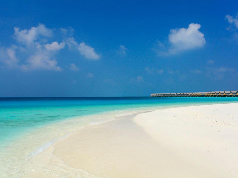 Weißer Sandstrand mit türkisfarbenem Wasser und klarem blauem Himmel.