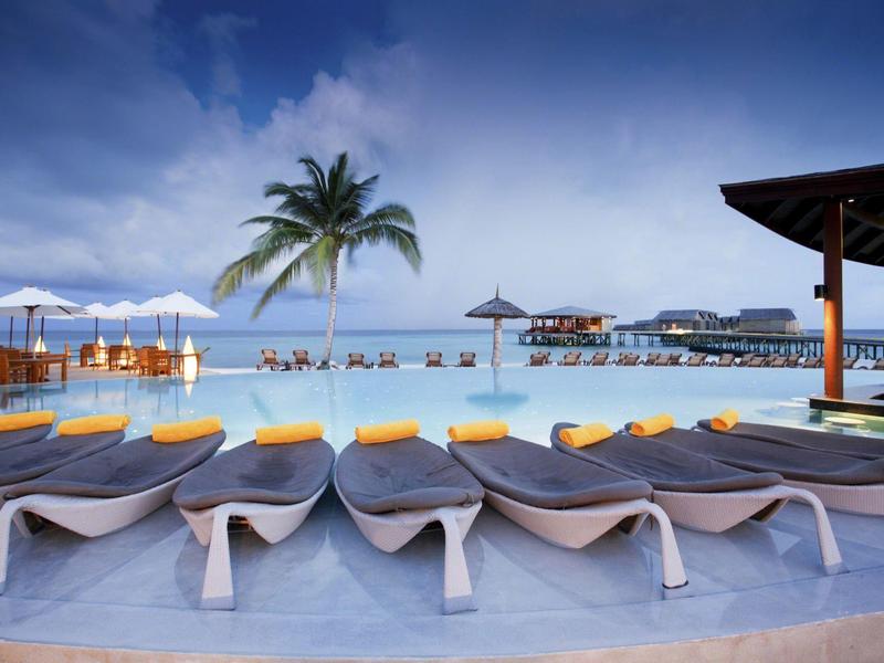 Luxuriöse Poollandschaft mit Liegestühlen, Palmen und Sonnenschirmen unter blauem Himmel