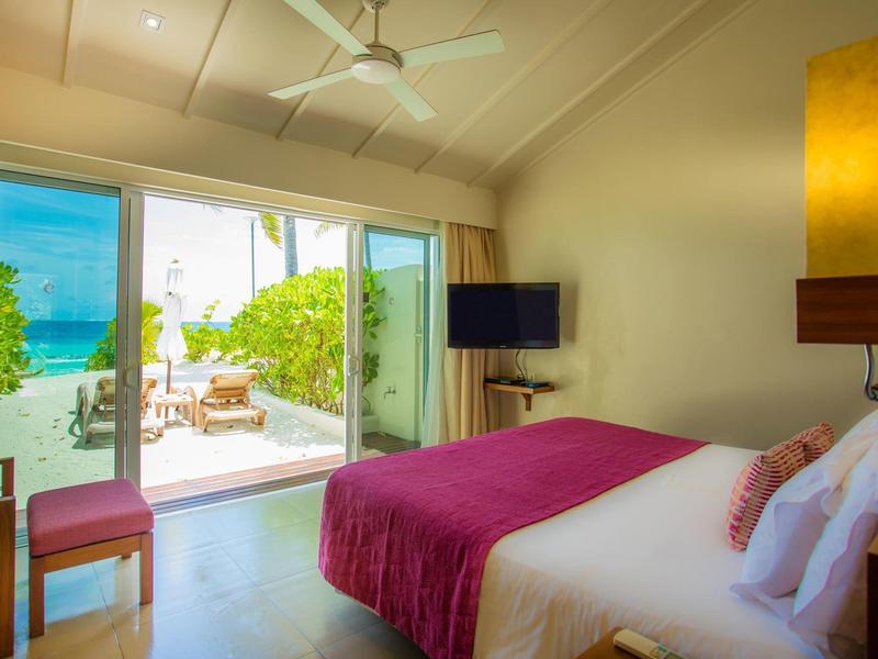 Helles Hotelzimmer mit Doppelbett, pinker Decke und Blick auf Terrasse mit Meer.
