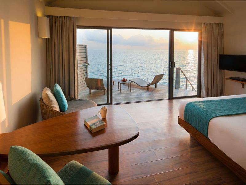 Helles Hotelzimmer mit Meerblick, Terrasse, Liegestühlen und modernem Interieur.