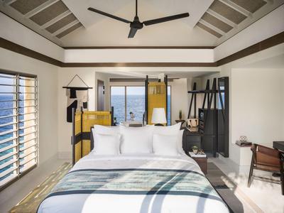 Modernes Hotelzimmer mit großem Bett, Deckenventilator und Meerblick durch große Fenster.