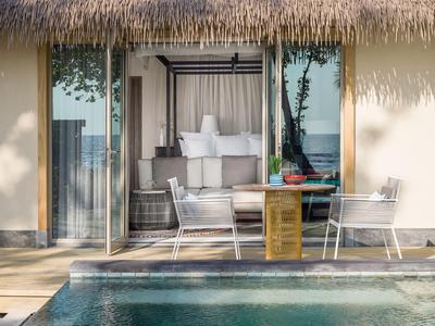 Moderner Außenbereich mit Pool, Terrasse und gemütlicher Sitzgruppe vor einer Hotel-Suite mit Glasfront.