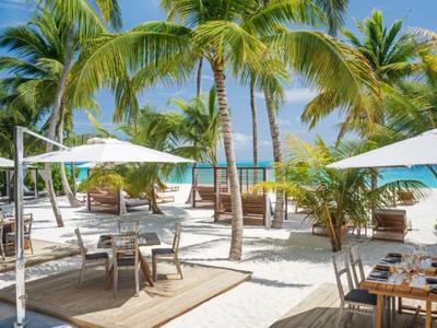 Strandrestaurant mit Sonnenschirmen und Palmen am Meer bei klarem Himmel.