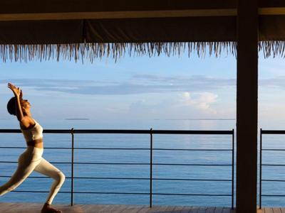 Frau macht Yoga auf einer Terrasse mit Meerblick bei klarem Himmel.