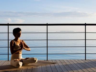 Frau praktiziert Yoga auf einer Holzterrasse mit Blick auf das Meer bei Sonnenuntergang.