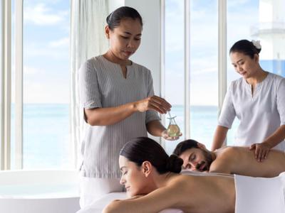 Zwei Masseure geben Paarmassage vor großen Fenstern mit Meerblick in einem hellen Raum.