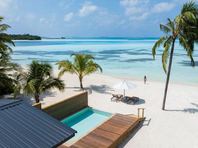 Ein tropischer Strand mit Palmen, weißem Sand und klarem blauem Wasser neben einer Terrasse mit Pool.