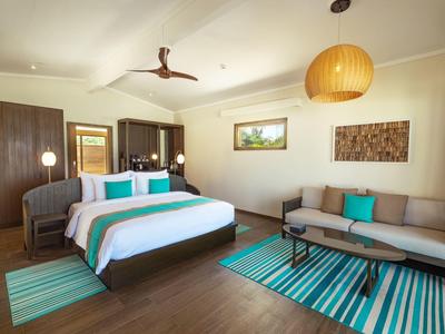 Modern eingerichtetes Hotelzimmer mit Doppelbett, Sofa und hellen Teppichen auf Holzboden.