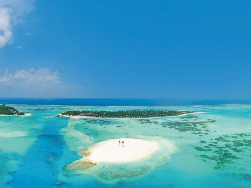 Panoramablick auf eine tropische Insel mit weißem Sand und klarem blauem Wasser unter blauem Himmel.
