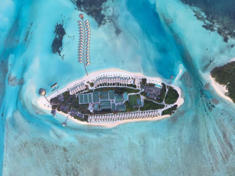 Luftaufnahme einer Insel mit einem großen Resort umgeben von klarem, blauem Wasser.