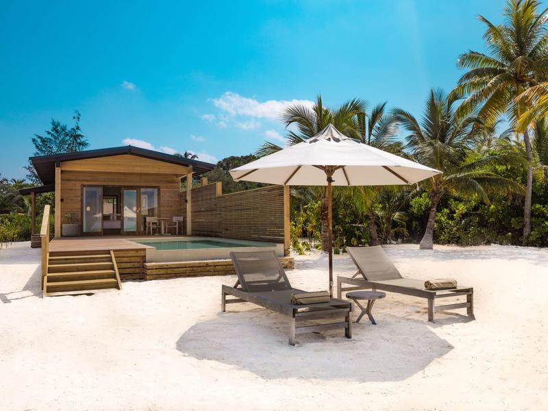 Strandresort mit Sonnenschirm, Liegestühlen und Holzhütte bei sonnigem Wetter.