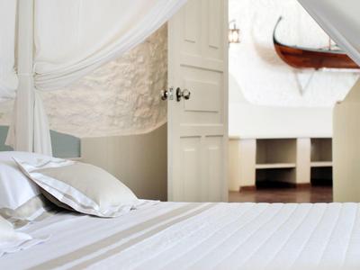 Weißes Schlafzimmer mit Himmelbett, glatten weißen Textilien und Blick auf geöffneten Raum.