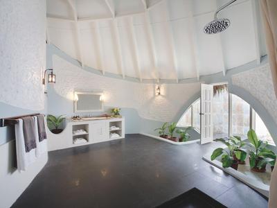 Bagno luminoso con grande soffitto rotondo, doccia, piante e asciugamani alla parete.