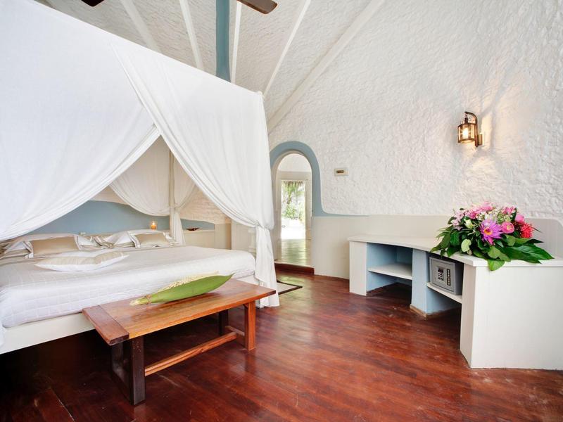 Helles Schlafzimmer mit Himmelbett, Holzboden und Blumen auf weißem Sideboard.
