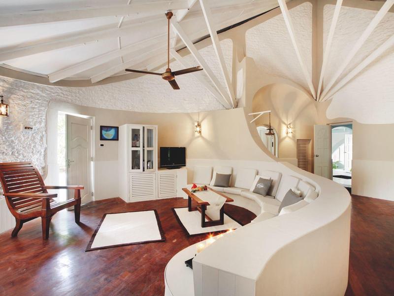 Helles Wohnzimmer mit geschwungener weißer Couch, Holzboden, Treppe und Deckenventilator.