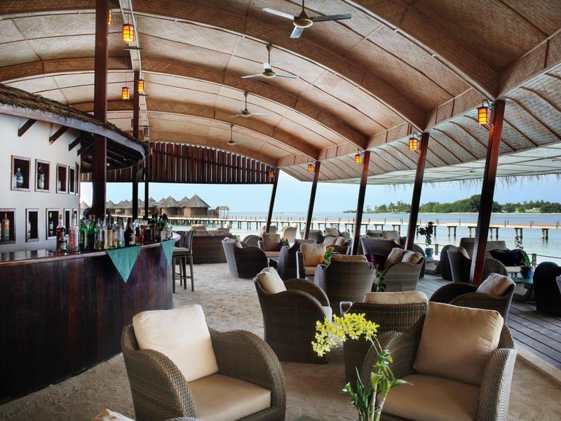 Großer, überdachter Außenbereich mit Lounge-Sesseln, Holzmöbeln und Blick aufs Wasser bei Tageslicht.