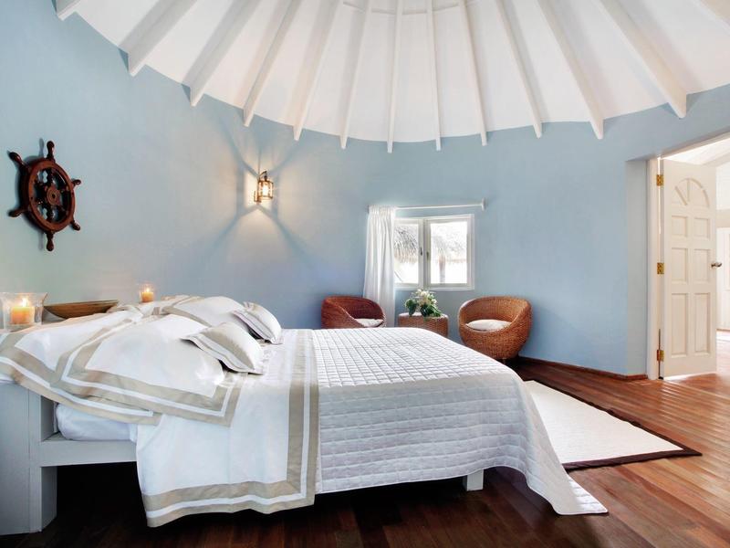 Hellblaues Schlafzimmer mit rundem weißen Dach, Holzboden, Doppelbett und Ledersesseln am Fenster.