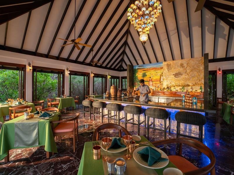 Gemütliches Restaurant mit grün eingedeckten Tischen, Holzmöbeln und einer farbenfrohen Wanddekoration.