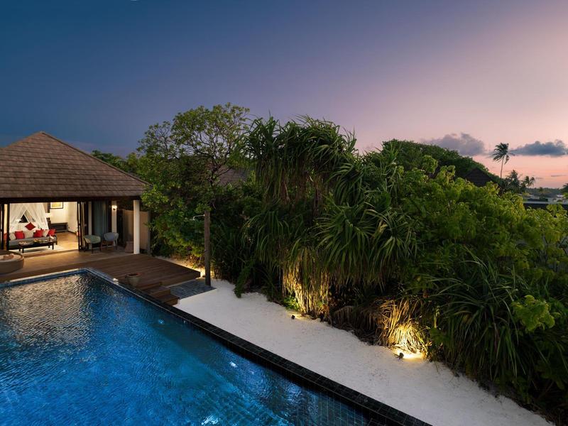 Luxuriöse Villa mit beleuchtetem Pool, tropischen Pflanzen und abendlichem Himmel im Hintergrund.