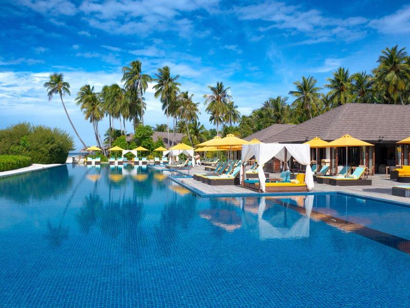 Großer Pool mit Liegen, Palmen und blauem Himmel in einem tropischen Resort.