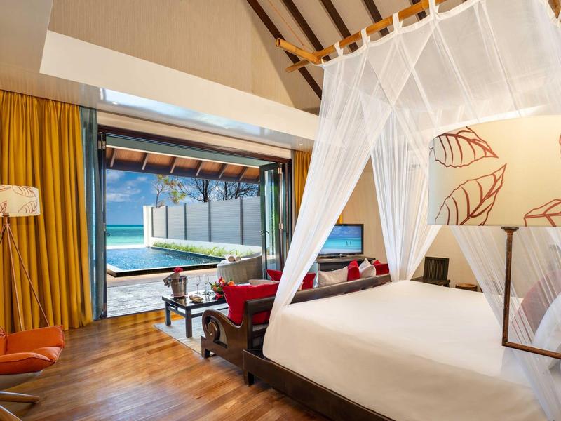 Helles Schlafzimmer mit vierposter Bett, Holzfußboden, orangenen Vorhängen und Poolblick durch offene Tür.