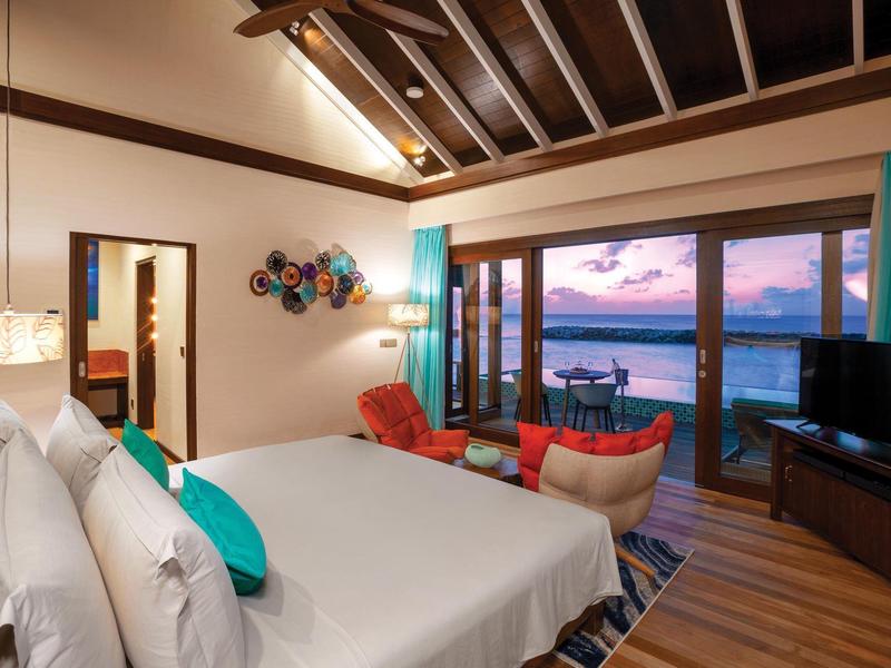 Helles Schlafzimmer mit großem Bett, bunten Stühlen, TV und Meerblick durch große Fenster.