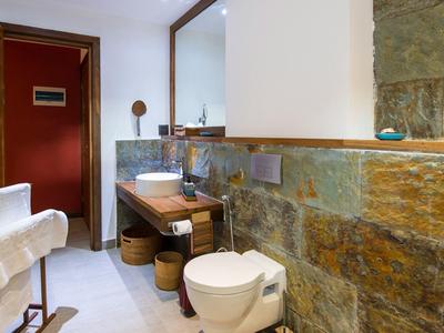 Moderner Badezimmer mit rustikaler Natursteinwand, Holzwaschtisch und weißer Toilette.