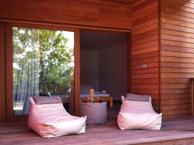 Kleine Holzveranda mit zwei weißen Sitzsäcken und kleinem grauem Tisch, großer Glas-Schiebetür.