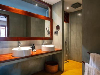 Moderner Badbereich mit zwei weißen Waschtischen auf Holzplatte, Spiegel und Regenbrause in Duschkabine.