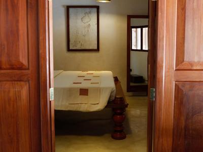 Blick durch eine geöffnete Holztür auf ein einfaches, rustikales Schlafzimmer mit Bett und Bild an der Wand.