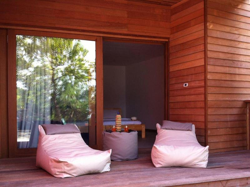 Kleine Holzveranda mit zwei weißen Sitzsäcken und kleinem grauem Tisch, großer Glas-Schiebetür.