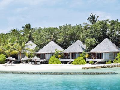 Bungalow con tetto di paglia su una spiaggia di sabbia bianca circondata da palme e acqua turchese.
