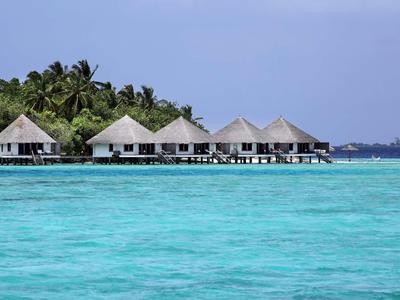 Überwasser-Bungalows mit Palmengarten im Hintergrund und türkisblauem Meer im Vordergrund.