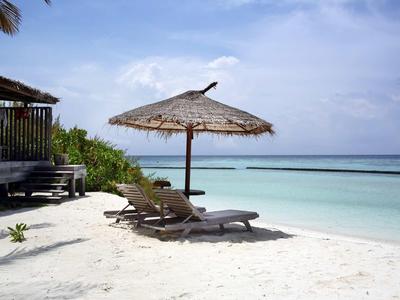 Leerer Strand mit weißen Sand, zwei Liegestühlen und einem Strohmusterschirm am türkisfarbenen Meer.