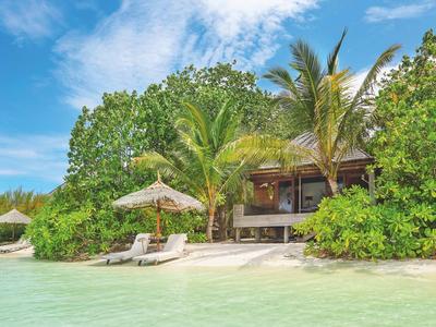 Tropisches Strandhaus mit Palme, Sandstrand und klarem türkisfarbenem Wasser unter blauem Himmel.