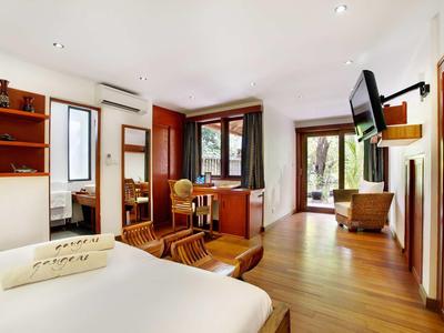 Helles, modernes Zimmer mit Holzboden, Doppelbett, TV an der Wand und einer Sitzecke.