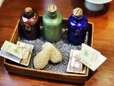 Drei farbige Flaschen, Seifenstücke und kleine Papiere liegen in einem Korb auf Holztisch.