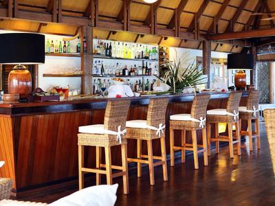 Heller, offener Barbereich mit Holztheke, hohen Stühlen und Regalen voller Flaschen.