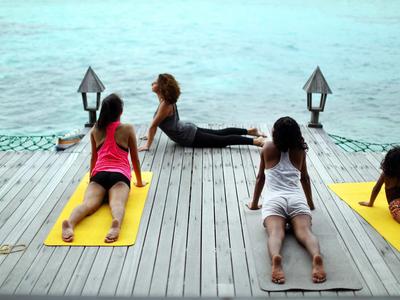 Trzy osoby uprawiające jogę na drewnianym pomoście nad spokojną wodą.