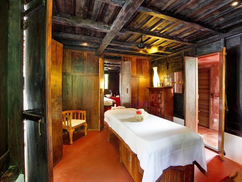 Gemütlicher Massageraum mit Holzbalken, warmem Licht und weiß gedeckter Liege.