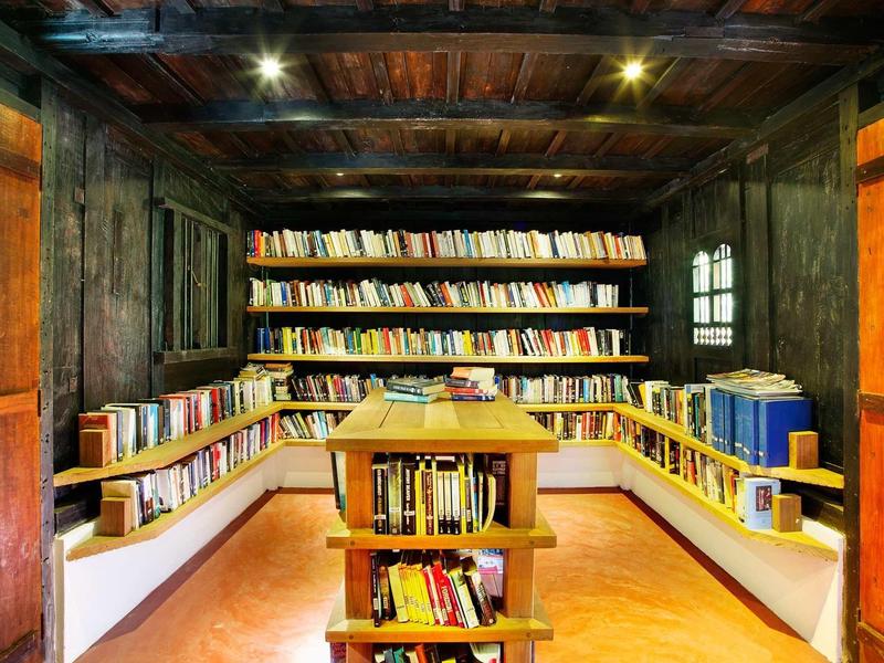 Kleine gemütliche Bibliothek mit vielen Büchern in dunklem Holzregal und warmem Licht.