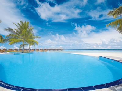 Großer blauer Infinity-Pool mit Palmen, blauem Himmel und Wolken am tropischen Strand.