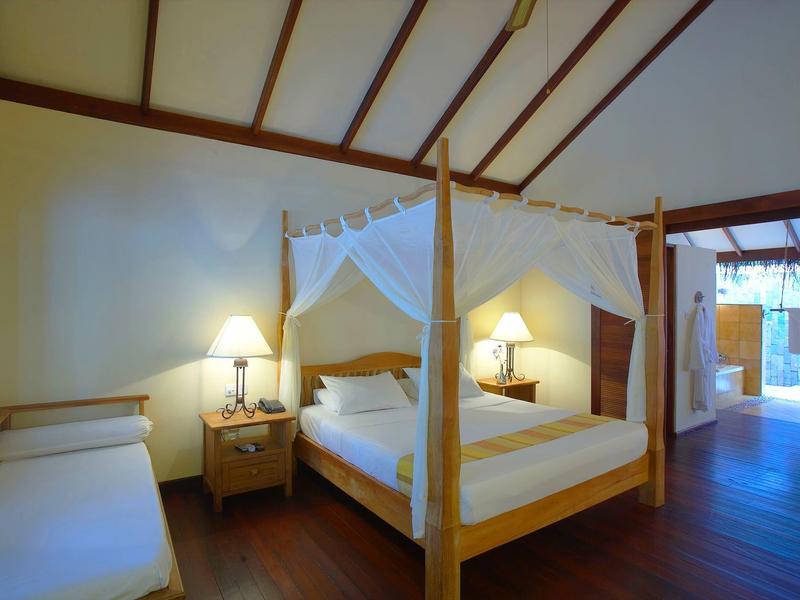 Hell eingerichtetes Schlafzimmer mit Himmelbett, Holzboden und zwei Nachttischlampen.