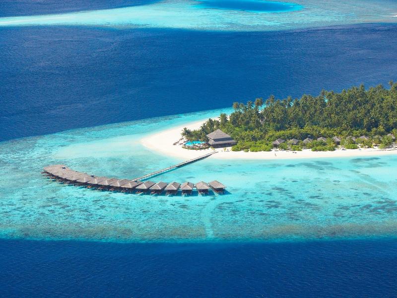 Kleine Insel mit weißem Sandstrand, Palmen und Stelzenhäusern im türkisblauen Meer.