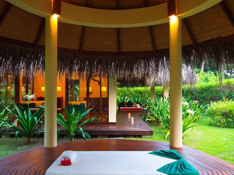 Offener Spa-Bereich mit Massagebett, Holzsäulen und Blick auf grünen Garten.